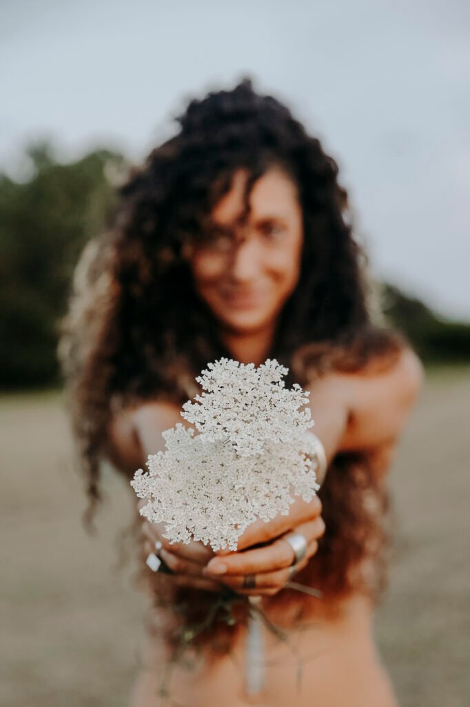 Portrait femme sauvage qui montre une fleurs et qui dit: qu’elle sait rester debout, se relever, et garder sa force malgré tout ce qui peut lui arriver